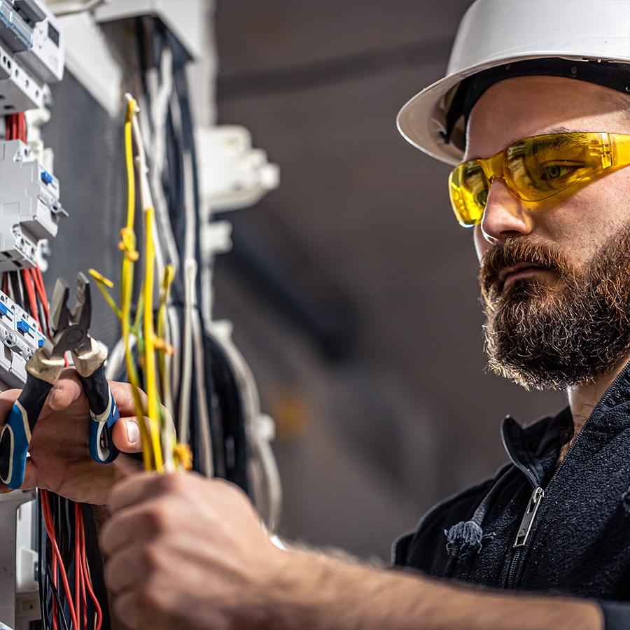 A man wearing a white helmet and yellow safety glasses works on an electrical conntecting cable